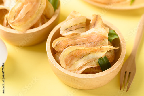 Banana chips or banana crisps in wooden bowl on yellow background, Delicious snack