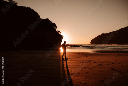 A silhouette of a person standing on the beach at sunset (ID: 484778475)