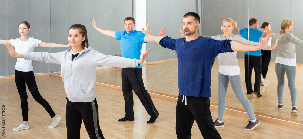 Group of sporty people doing stretching exercises before dance training in modern studio