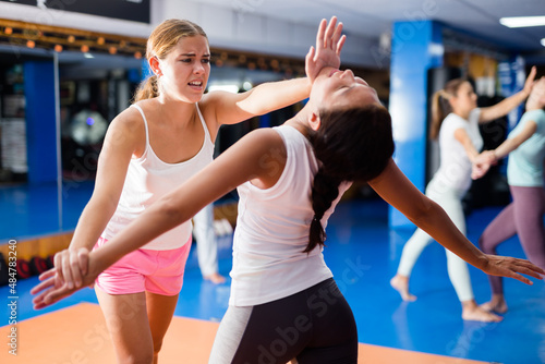Females are training self-defence moves in pairs in sporty gym with trainer