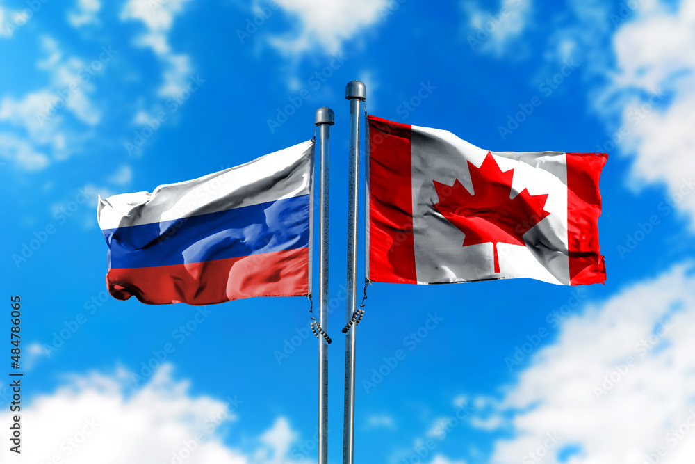 Flags of Russia and Canada on the wind against blue sky