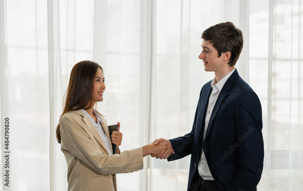 Young businessman and businesswoman shake hand together, smile, hold tablet, standing, wear suit. Young man and woman work business with home office background and copy space Young businessman and businesswoman shake hand together, smile, hold tablet, standing, wear suit. Young man and woman work business with home office background and copy space