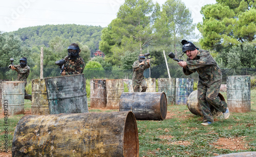 Dynamic paintball battle. Group of men and women in camouflage attacking opposite team