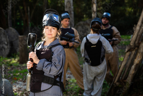 Young woman wearing uniform and holding gun ready for playing with friends on paintball outdoor