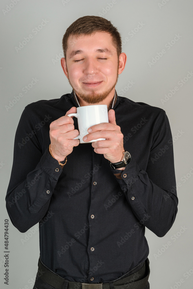 A bearded businessman in a black shirt enjoys the aroma of coffee holding a white mug with a hot drink in his hands A bearded businessman in a black shirt enjoys the aroma of coffee holding a white mug with a hot drink in his hands