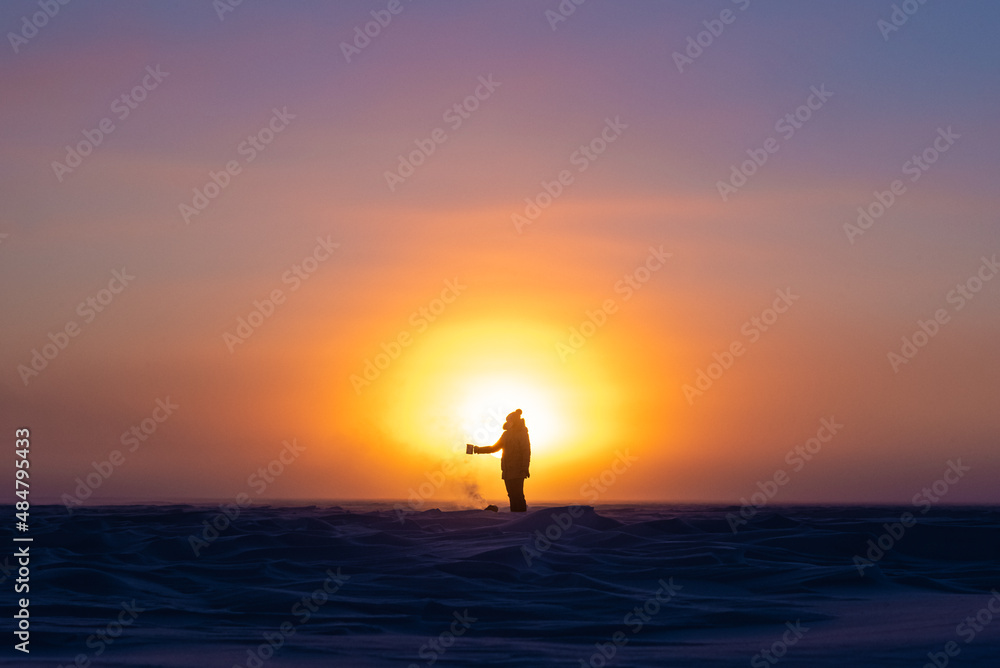 Beautiful arctic sunrise in northern Canada during peak wintertime. Woman silhouette standing in front of bright, blazing sun. 