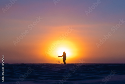 Beautiful arctic sunrise in northern Canada during peak wintertime. Woman silhouette standing in front of bright  blazing sun. 