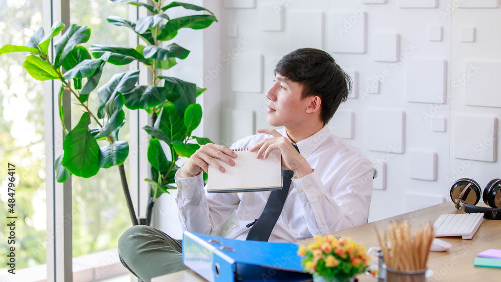 Portrait studio shot of Asian professional successful male businessman employee in formal shirt with necktie sitting look at camera at working desk with computer monitor keyboard mouse and stationery Portrait studio shot of Asian professional successful male businessman employee in formal shirt with necktie sitting look at camera at working desk with computer monitor keyboard mouse and stationery