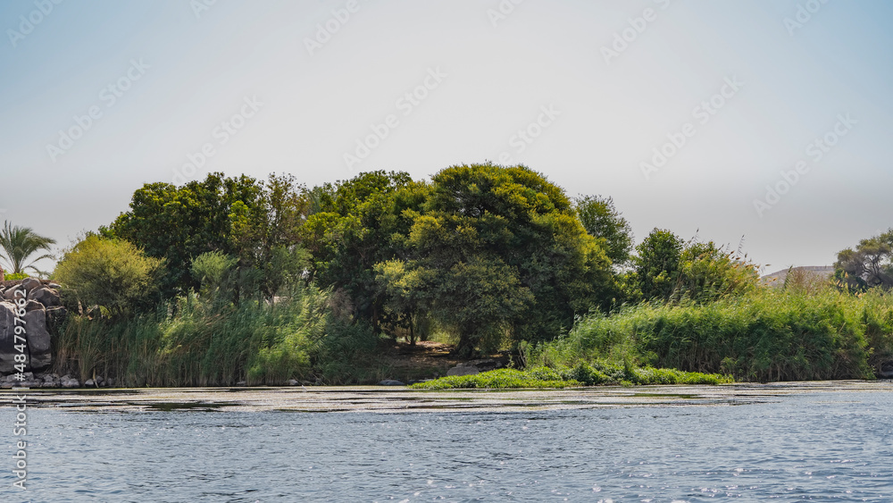 On the river bank there are thickets of reeds, picturesque boulders. The path winds between green trees. Blue sky. Egypt. Nile On the river bank there are thickets of reeds, picturesque boulders. The path winds between green trees. Blue sky. Egypt. Nile