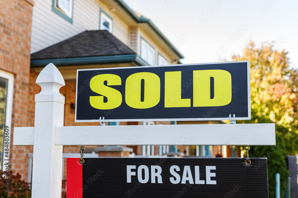 Sold yellow and black sign close-up in front of a house in a residential neighborhood