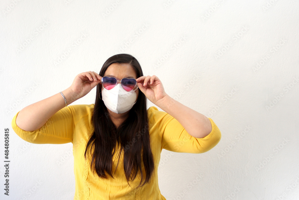 Latin adult woman with face mask and heart-shaped glasses excited for February Valentine's Day of Love and Friendship in the new normality due to the Covid-19 pandemic
