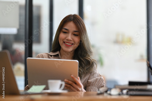 Pleased young businesswoman using digital tablet at modern office.