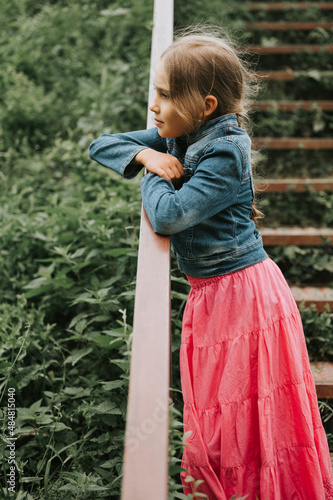 thoughtful candid eight year old kid girl stands on staircase with grass and enjoying nature. prepubertal age of children and their lives, mind psychology and mental health concept. fashion clothes photo