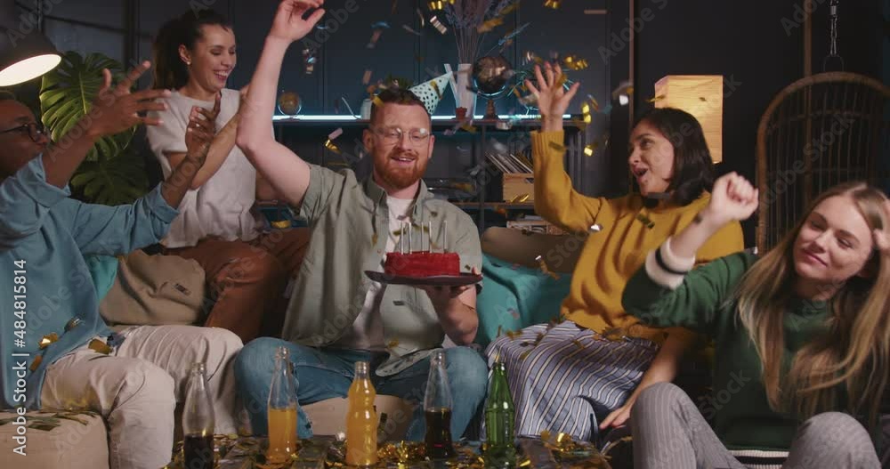 Happy excited smiling Caucasian redhead man holds birthday cake throwing confetti celebrating with multiethnic friends. Happy excited smiling Caucasian redhead man holds birthday cake throwing confetti celebrating with multiethnic friends.