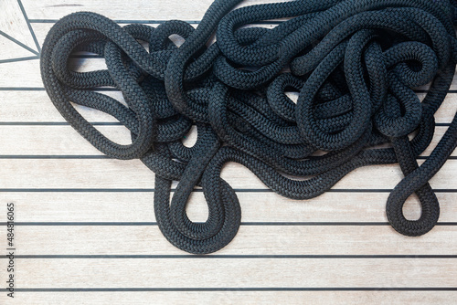 Pile of black rope on the teak deck of a yacht  top view.