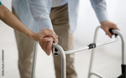 Unrecognizable senior man using walking aid, young female supporting and helping him at home, closeup view