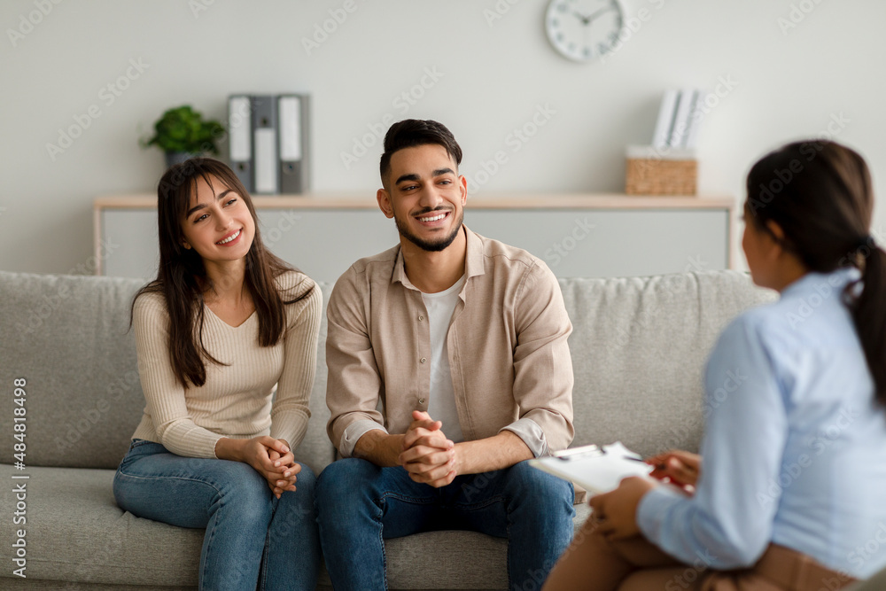 Family therapy. Happy middle eastern couple sitting on couch at counselor's office, listening advices and smiling Family therapy. Happy middle eastern couple sitting on couch at counselor's office, listening advices and smiling