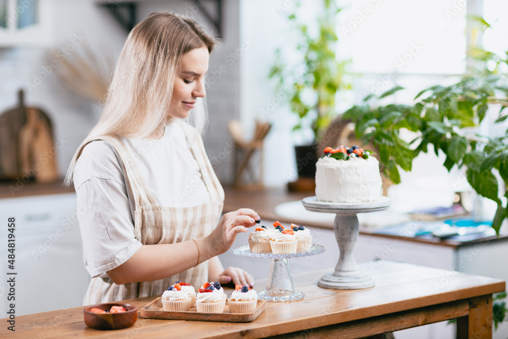 Pastry chef confectioner young caucasian woman decorate cake on kitchen table. Cakes cupcakes and sweet dessert Pastry chef confectioner young caucasian woman decorate cake on kitchen table. Cakes cupcakes and sweet dessert