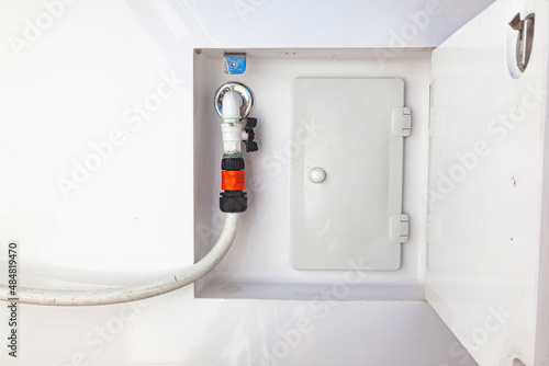 A water tap with a hose connected to it on the hull of the yacht. A place for water supply on a yacht. © Сергей Жмурчак