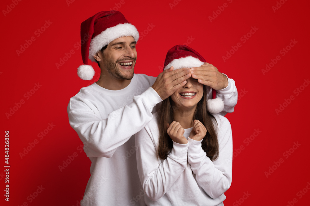 Guess Who. Playful Guy In Santa Hat Covering Girlfriend's Eyes With Hands Guess Who. Playful Guy In Santa Hat Covering Girlfriend's Eyes With Hands