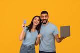 Joyful arab spouses with laptop and credit card celebrating success, emotionally reacting to online profit