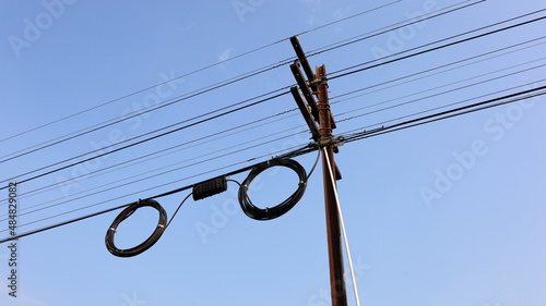 Black boxes and cable reels on poles. Internet box or splitter box with high-speed fiber optic cable hanging on a metal electric pole on a blue background with copy space. Selective focus