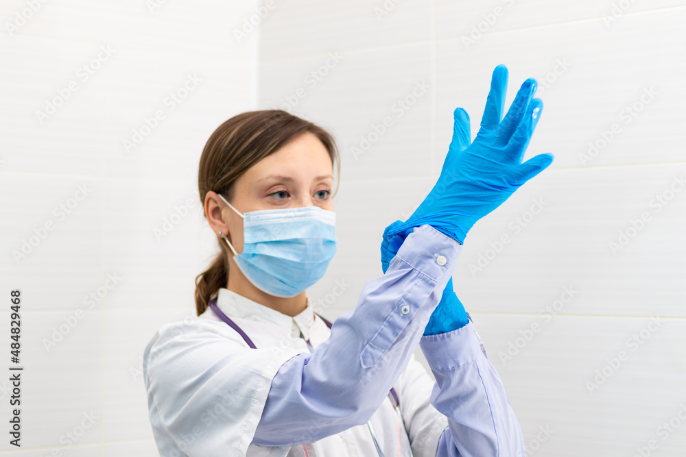 Beautiful young doctor woman in a medical mask and gloves with a stethoscope in a hospital during the coronavirus pandemic. Selective focus. Portrait. Close-up Beautiful young doctor woman in a medical mask and gloves with a stethoscope in a hospital during the coronavirus pandemic. Selective focus. Portrait. Close-up