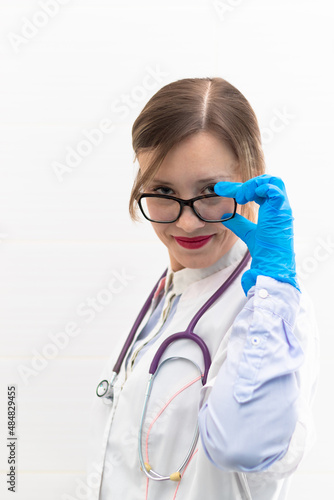 Beautiful young doctor woman in medical gloves and glasses with a stethoscope in a hospital on a white background. Selective focus. Portrait. Close-up