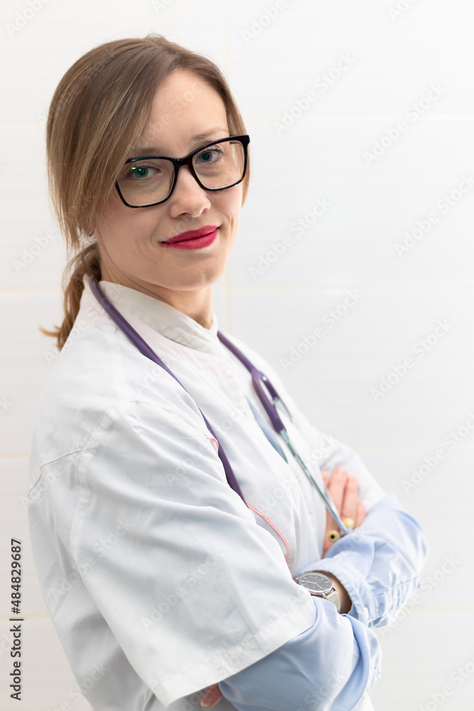 Beautiful young doctor woman in a medical coat and glasses with a stethoscope in a hospital on a white background. Selective focus. Portrait. Close-up Beautiful young doctor woman in a medical coat and glasses with a stethoscope in a hospital on a white background. Selective focus. Portrait. Close-up
