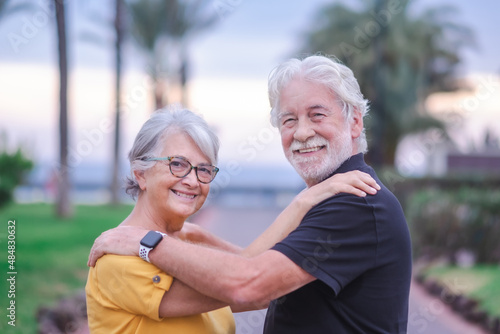 Happy Elderly adult mature couple in love. Senior husband and wife in outdoors at sunset hugging and bonding with true emotions. Carefree cheerful retired couple looking at camera enjoying wellbeing