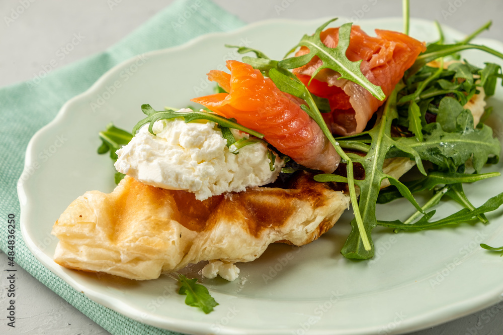 Croffles with salmon and cheese and arugula in a plate close-up. Croissant and waffle in one dish. Croffles with salmon and cheese and arugula in a plate close-up. Croissant and waffle in one dish.