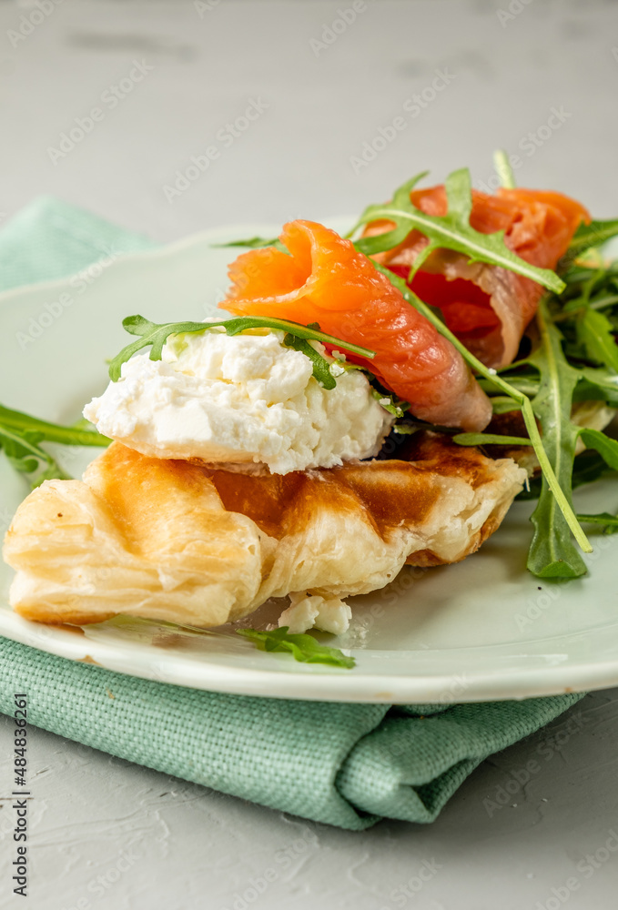 Croffles with salmon and soft cheese, arugula in a plate close-up. Croissant and waffle in one dish. Croffles with salmon and soft cheese, arugula in a plate close-up. Croissant and waffle in one dish.