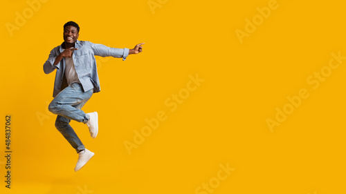 Emotional african american millennial man jumping  pointing at copy space