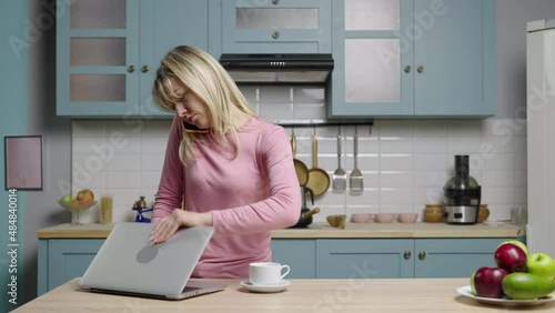 Young woman is working on laptop, talking on phone and is very upset. Family bloggers filming stories in kitchen for social media and life video blog. Slow motion ready, 4K at 59.97fps. photo