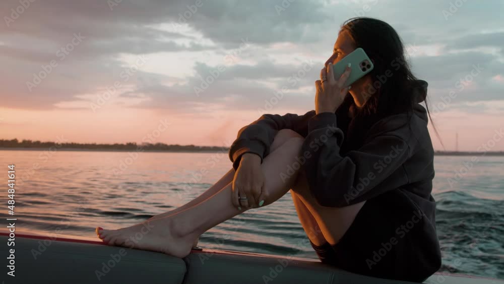 A woman is talking on the phone at sunset in a motor boat A woman is talking on the phone at sunset in a motor boat