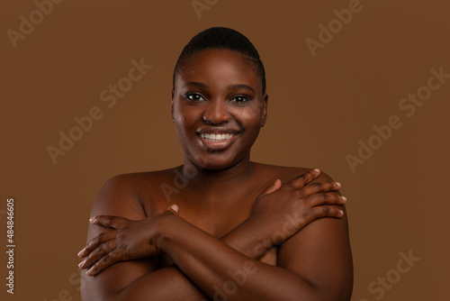 Curvy African American woman with acne embracing herself