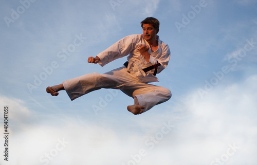 Yoko Tobi Geri, Karate, Kampfsportler fliegt durch die Luft, Martial Arts vor weißen Wolken und blauem Himmel mit Abendlicht photo