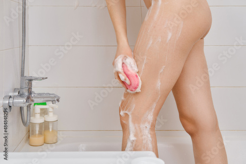 Cropped image of a woman washing her legs with sponge in the bathroom