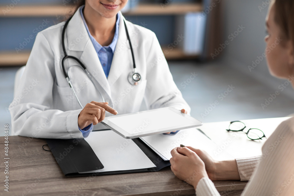 Cheerful young hindu female doctor in white coat with stethoscope shows tablet with results of exam in office clinic Cheerful young hindu female doctor in white coat with stethoscope shows tablet with results of exam in office clinic