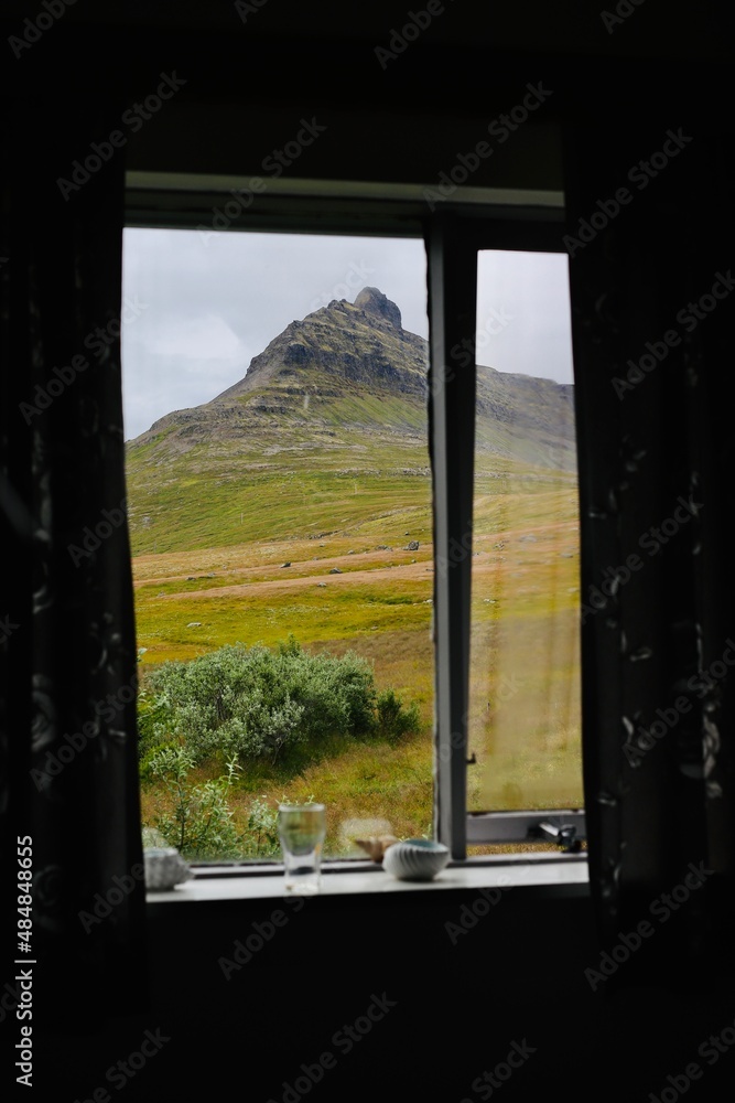 A cosy window view of a mountain from a dark room on a cloudy day