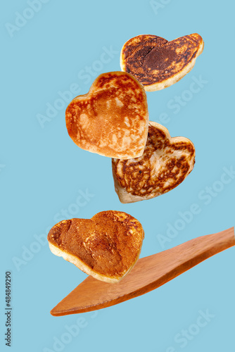 flying heart shaped pancakes over wooden kitchen spatula on blue background photo