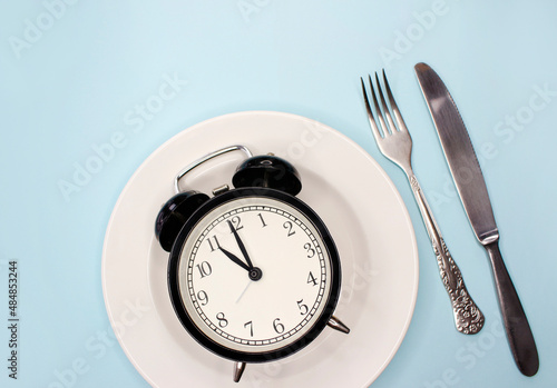 Concept of intermittent fasting, ketogenic diet, weight loss. fork and knife, alarmclock on plate