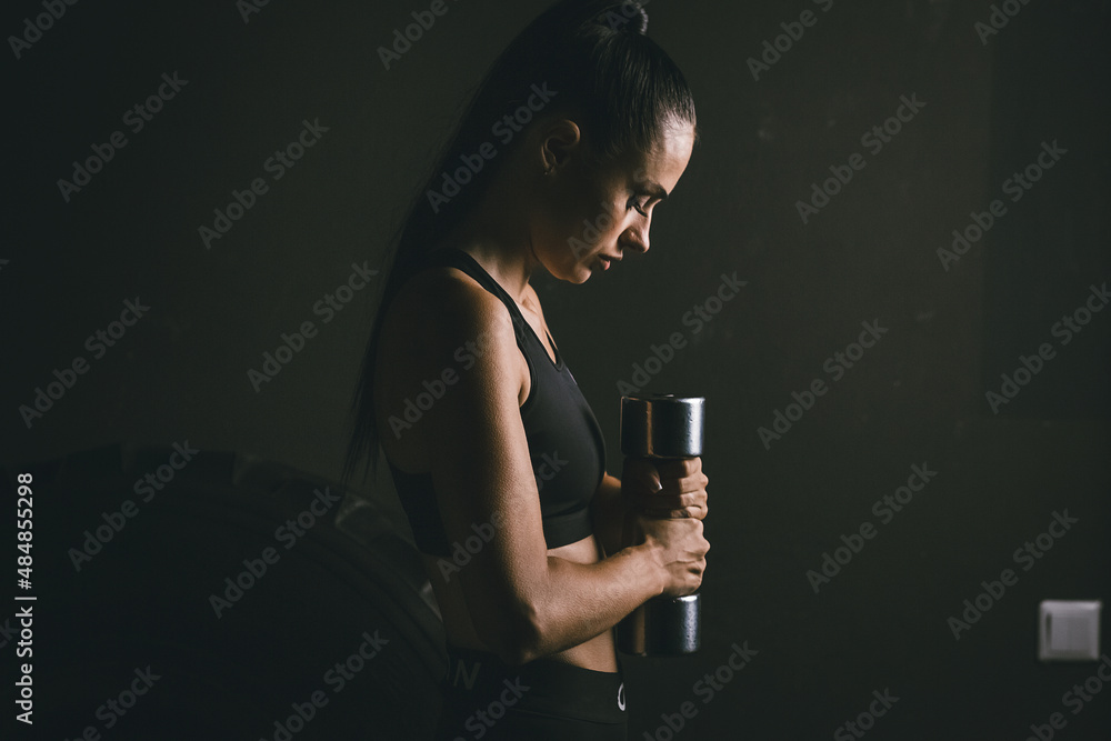 Young woman in a tracksuit with dumbbells in her hands. Side view Young woman in a tracksuit with dumbbells in her hands. Side view