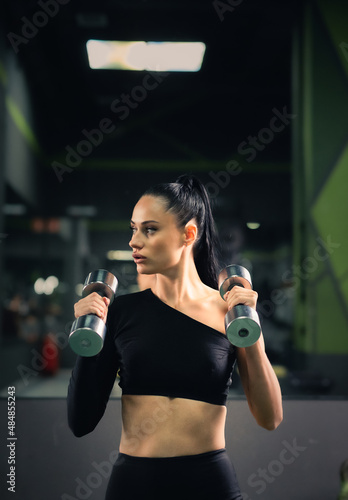 Modern young woman in a sports top with dumbbells in her hands on the background of the gym