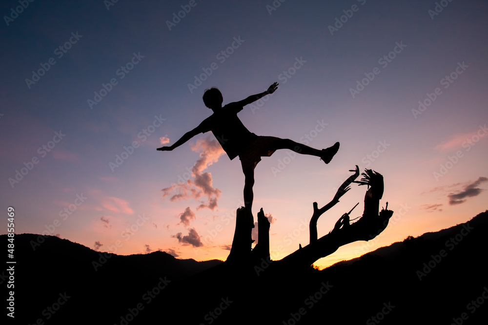silhouette of a young boy on a log Surrounded by shadows of mountains Atit falls in the evening feeling refreshed after exercise There is space for messages in the sky.