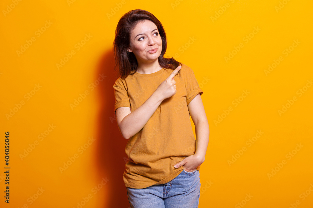 Positive adult using index finger to point at right side of studio. Young person pointing aside and standing over isolated background while posing for camera. Caucasian woman smiling Positive adult using index finger to point at right side of studio. Young person pointing aside and standing over isolated background while posing for camera. Caucasian woman smiling
