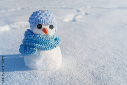 Little cute snowman in a knitted blue hat and scarf on snow on a sunny winter day. Christmas card  © isavira