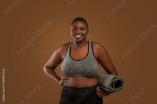 Chubby black woman holding yoga mat at studio