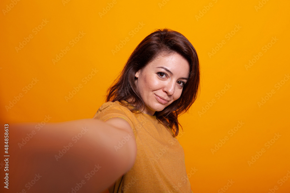 POV of positive woman holding camera to take selfie in studio. Cheerful adult taking photograph and smiling while standing over isolated background. Casual person taking picture with device POV of positive woman holding camera to take selfie in studio. Cheerful adult taking photograph and smiling while standing over isolated background. Casual person taking picture with device