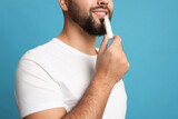Young man applying lip balm on turquoise background, closeup